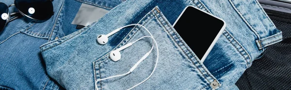 Крупный план мобильного телефона в кармане джинсов возле наушников и солнцезащитных очков, баннер — стоковое фото
