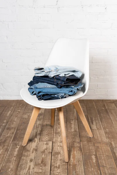 Chair with stacked denim garments on wooden floor near white brick wall — Stock Photo