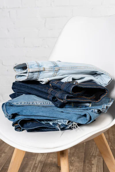 Pile de différents vêtements en denim sur chaise blanche près du mur de briques — Photo de stock