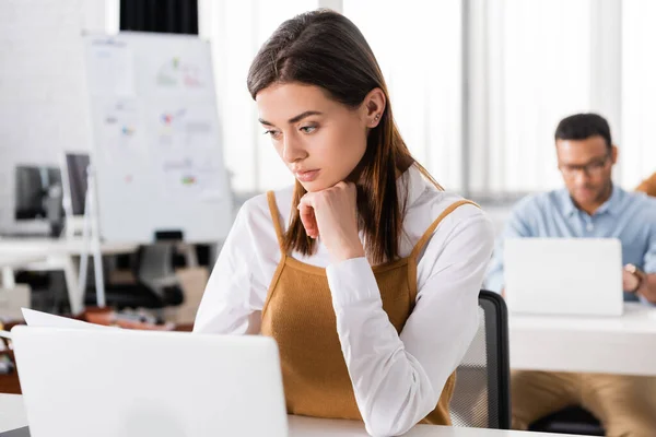 Geschäftsfrau sitzt neben Laptop auf verschwommenem Vordergrund im Büro — Stockfoto