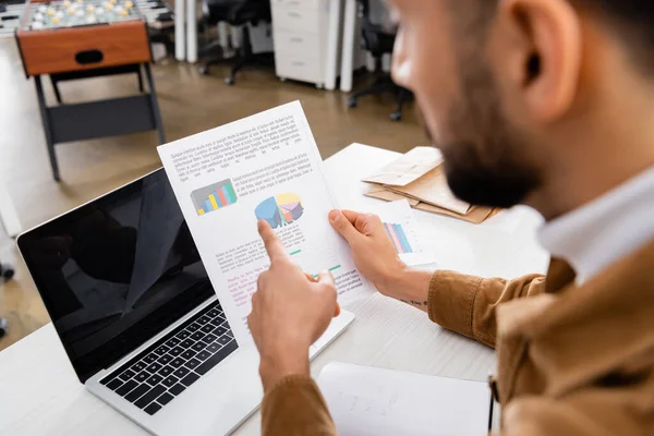 Ausgeschnittene Ansicht von Geschäftsmann zeigt auf Diagramme auf Dokument in der Nähe Laptop im Büro — Stockfoto