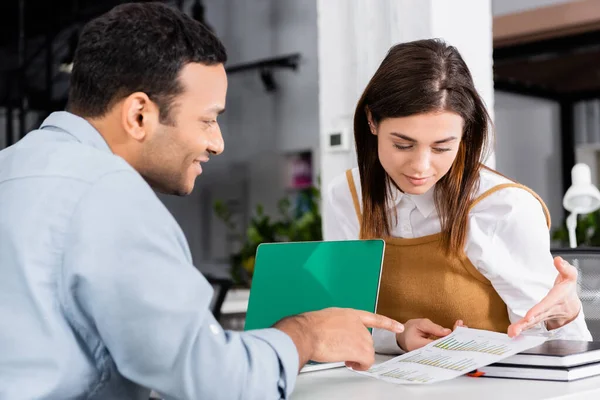 Businesswoman pointing at document near smiling indian colleague on blurred foreground — Stock Photo