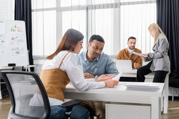 Multiethnische Geschäftsleute arbeiten mit Papieren in der Nähe von Kollegen im Büro — Stockfoto