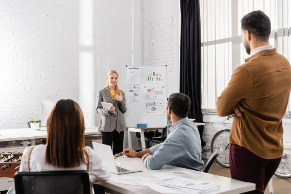 Smiling businesswoman with digital tablet looking at colleagues on blurred foreground in office — Stock Photo