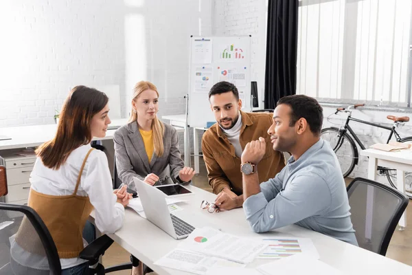 Empresarios multiculturales hablando cerca de dispositivos y papeles en la oficina - foto de stock