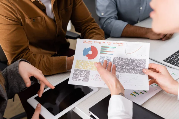 Vista recortada de la mujer de negocios apuntando a gráficos cerca de colegas y dispositivos en la oficina - foto de stock