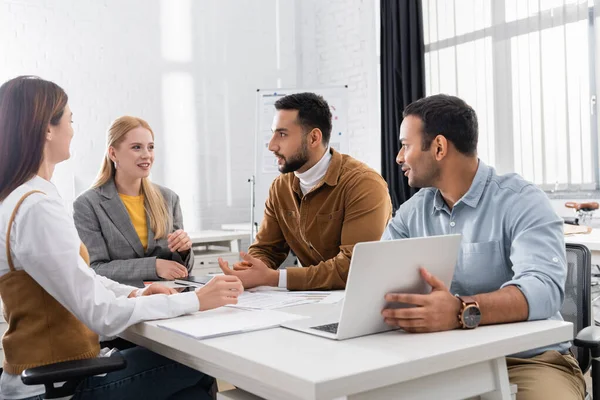 Lächelnde multikulturelle Geschäftsleute reden neben Laptop und Papieren — Stockfoto