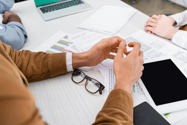 Ausgeschnittene Ansicht eines Geschäftsmannes, der neben einem digitalen Tablet sitzt, Zeitungen und Kollegen auf verschwommenem Hintergrund — Stockfoto