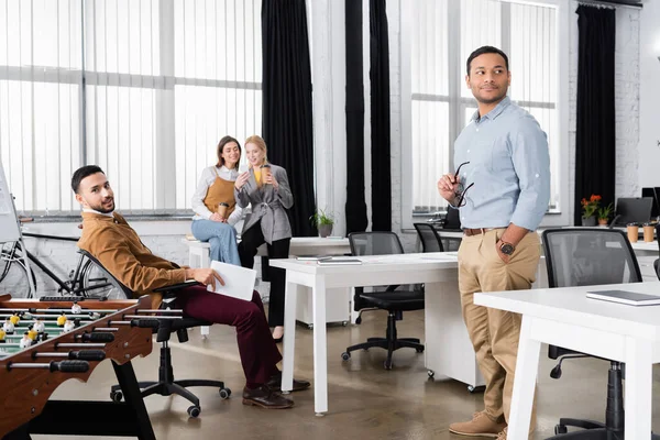 Multiethnic businesspeople standing near table soccer in office — Stock Photo
