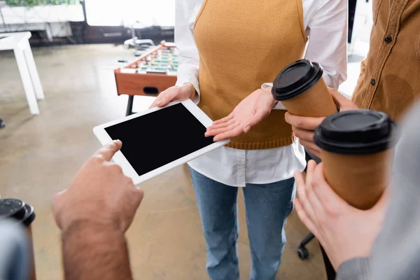 Cropped view of businessman pointing at digital tablet near colleagues with coffee to go — Stock Photo
