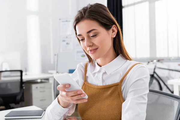 Positive businesswoman using smartphone in office — Stock Photo