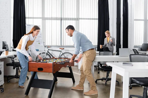 Cheerful businesswoman playing table soccer with indian colleague in office — Stock Photo