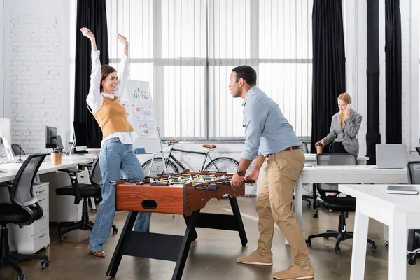 Happy businesswoman looking at indian colleague near table soccer in office — Stock Photo