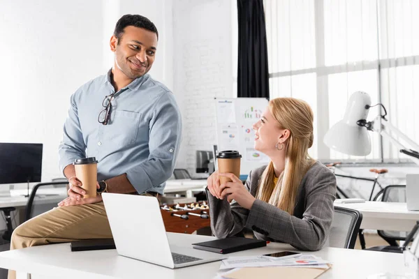 Hombre de negocios indio sonriente mirando a colega con café para ir en la oficina - foto de stock