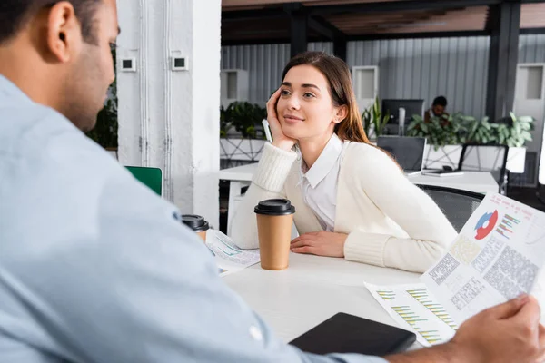 Mujer de negocios mirando a un colega indio con papeles en primer plano borroso - foto de stock