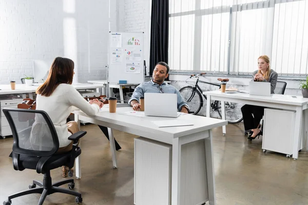 Мультиэтнические бизнесмены разговаривают возле кофе, чтобы пойти и ноутбуки в офисе — стоковое фото