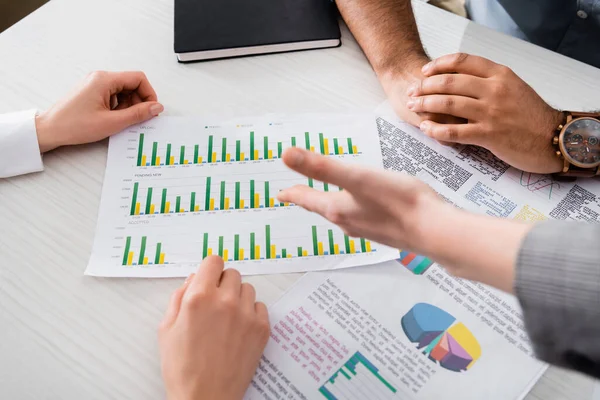 Vista recortada de gente de negocios trabajando con gráficos en papeles cerca del cuaderno en la mesa - foto de stock