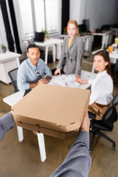 Delivery man holding pizza boxes near multiethnic businesspeople on blurred background — Stock Photo