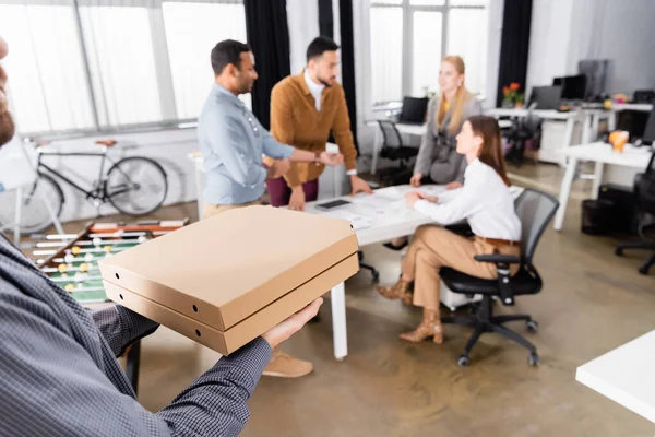 Delivery man holding pizza boxes near business people on blurred background in office — Stock Photo