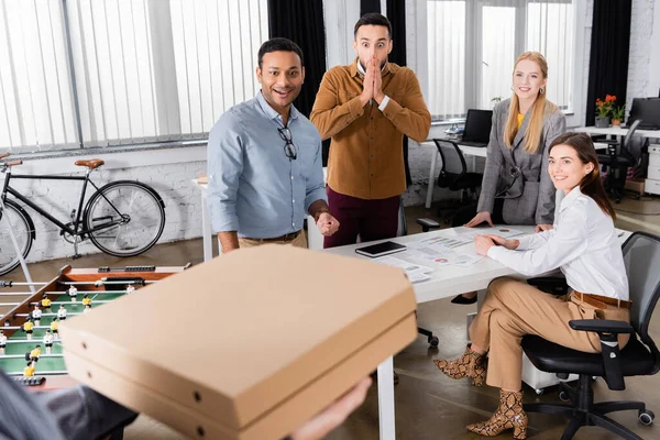 Gente de negocios sonrientes mirando mensajero con cajas de pizza sobre fondo borroso - foto de stock