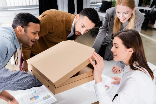 Lächelnde multiethnische Geschäftsleute, die im Büro in der Nähe von Zeitungen Pizza anschauen — Stockfoto