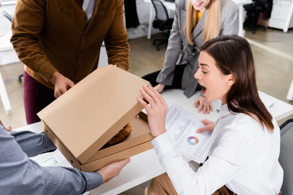 Excited businesswoman looking at pizza near colleagues and courier in office — Stock Photo