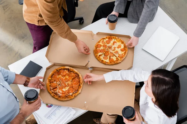 Overhead view of business people with coffee to go taking pizza in office — Stock Photo