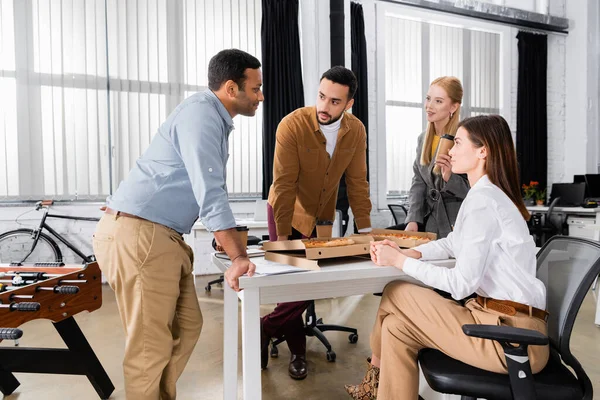 Multicultural business people talking near pizza during lunch in office — Stock Photo