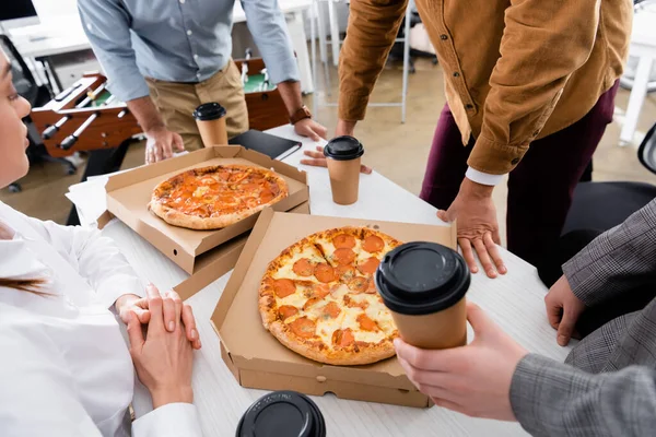 Empresária sentada perto de colegas com bebida takeaway e pizza saborosa no escritório — Fotografia de Stock