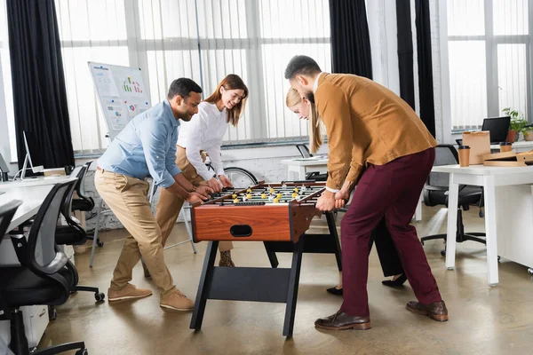 Des hommes d'affaires multiethniques souriants jouant au baby-foot au bureau — Photo de stock