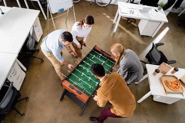 Overhead view of multicultural business people playing table soccer during lunch in office — Stock Photo