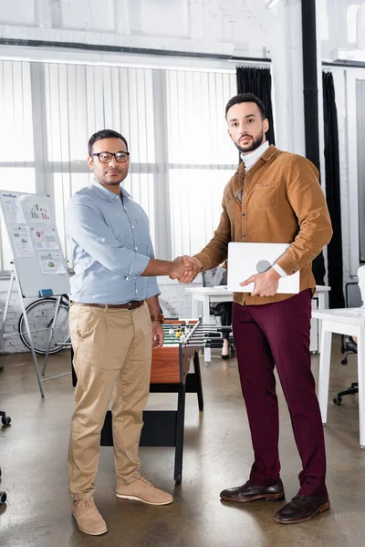 Multiethnic businessmen with laptop handshaking in office — Stock Photo