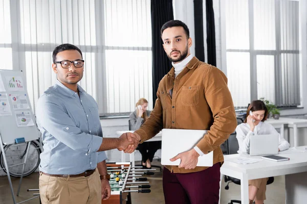 Multiethnische Geschäftsleute beim Händeschütteln und Blick in die Kamera im Büro — Stockfoto