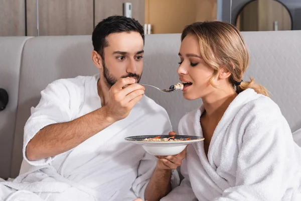 Homem árabe em roupão de banho alimentando salada para namorada na cama do hotel — Fotografia de Stock