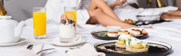 Ausgeschnittene Ansicht von leckerem Frühstück und Getränken auf dem Bett nahe Paar auf verschwommenem Hintergrund im Hotel, Banner — Stockfoto