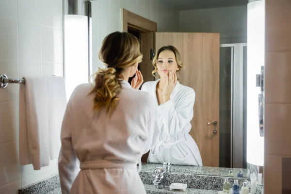Vista posteriore della donna bionda che guarda lo specchio nel bagno dell'hotel — Foto stock