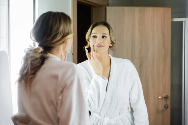 Back view of smiling woman with hand near cheek looking at mirror in hotel — Stock Photo