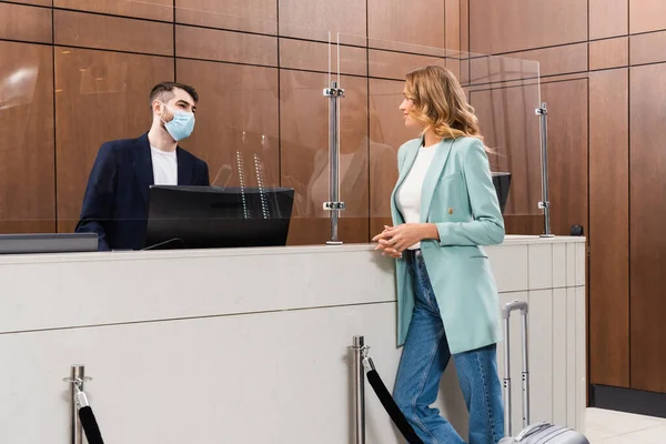 Giovane donna in piedi vicino direttore dell'hotel in maschera medica nella hall — Foto stock