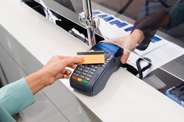 Vista cortada de recepcionista segurando terminal de pagamento perto de mulher com cartão de crédito no hotel — Fotografia de Stock