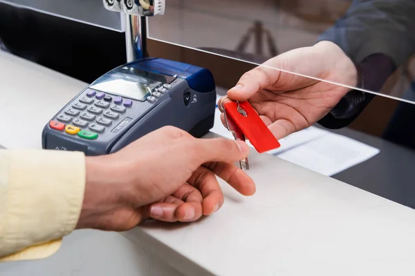 Vue recadrée du gestionnaire donnant la clé à l'homme au premier plan flou près du terminal de paiement dans le hall de l'hôtel — Photo de stock