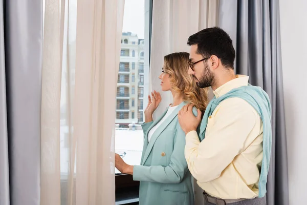 Vue latérale du couple interracial regardant la fenêtre dans la chambre d'hôtel — Photo de stock