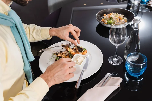 Vista recortada del hombre sentado cerca de deliciosos camarones en el plato en la habitación de hotel - foto de stock