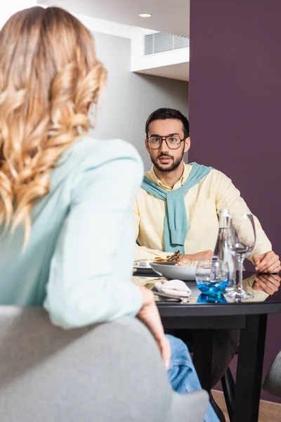 Muslim man talking to girlfriend on blurred foreground near food on table in hotel — Stock Photo