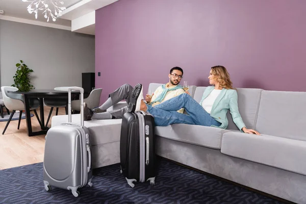 Suitcases near interracial couple holding glasses of wine in hotel room — Stock Photo