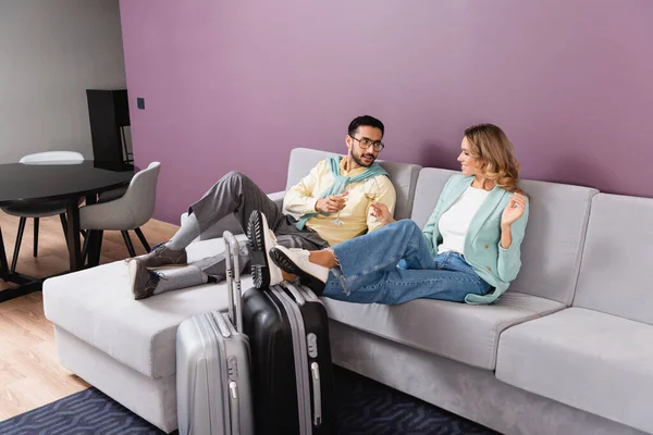 Interracial couple holding wine glasses near luggage in hotel — Stock Photo