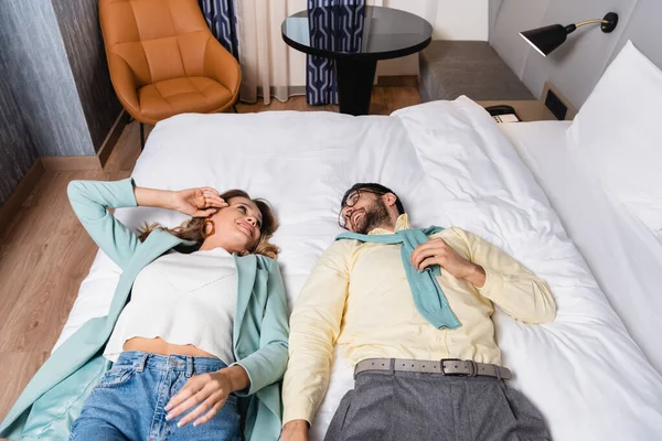 Высокий угол обзора улыбающейся межрасовой пары лежащей на кровати в отеле — стоковое фото