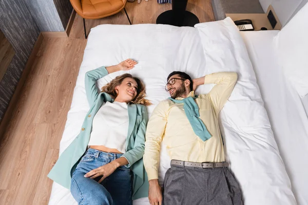 High angle view of cheerful interracial couple looking at each other while lying on hotel bed — Stock Photo