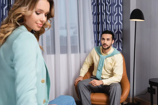 Homem árabe olhando para a namorada em primeiro plano borrado enquanto sentado em poltrona — Fotografia de Stock