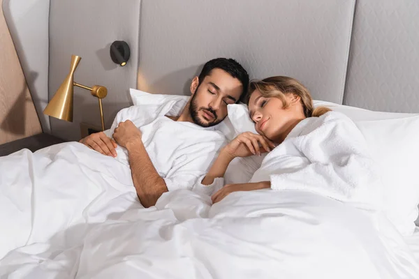 Молода міжрасова пара спить на білому ліжку в готелі — стокове фото