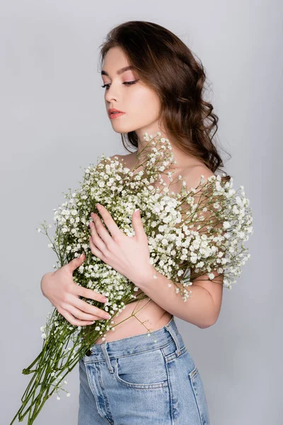 Junges Modell ohne Hemd posiert mit weißen Blüten auf grau — Stockfoto